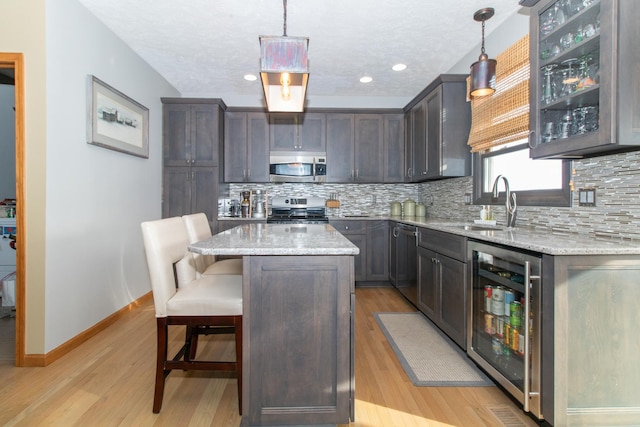 kitchen featuring backsplash, wine cooler, light stone counters, appliances with stainless steel finishes, and a sink