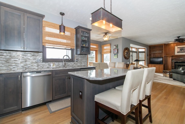 kitchen featuring dishwasher, a breakfast bar, a glass covered fireplace, a ceiling fan, and a sink