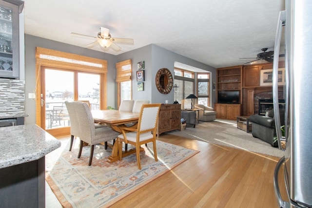 dining space with light wood-style floors, a glass covered fireplace, and a ceiling fan