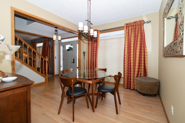 dining room featuring stairs, baseboards, light wood finished floors, and a chandelier