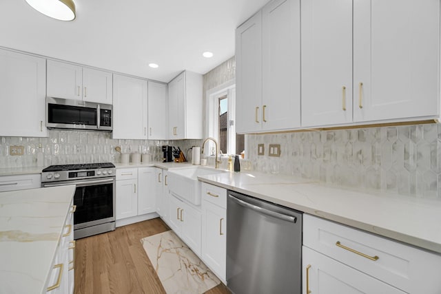 kitchen with stainless steel appliances, white cabinets, a sink, light stone countertops, and light wood-type flooring