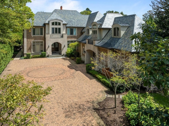 french country style house featuring a chimney, a high end roof, and stucco siding