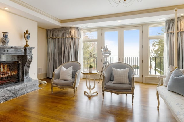 living area featuring light wood finished floors, visible vents, a premium fireplace, ornamental molding, and french doors