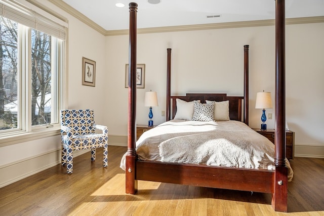 bedroom featuring baseboards, ornamental molding, visible vents, and light wood-style floors