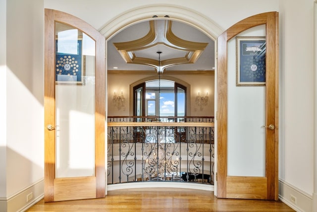 wine area with a chandelier, wood finished floors, a raised ceiling, and crown molding