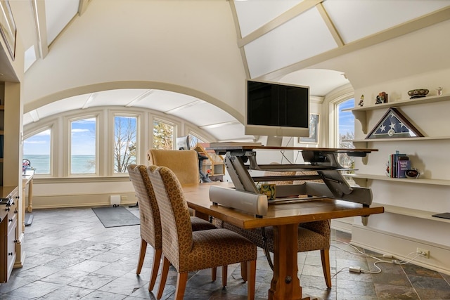 dining space with a water view, plenty of natural light, a towering ceiling, and stone tile flooring