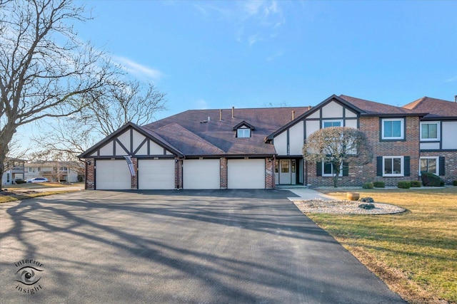 english style home with a front yard, driveway, stucco siding, a garage, and brick siding