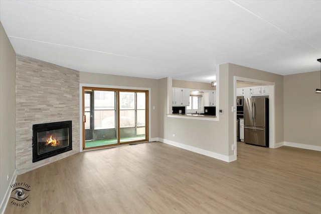 unfurnished living room with light wood-style flooring, a fireplace, and baseboards