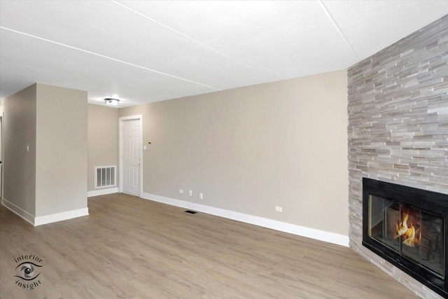 unfurnished living room with a large fireplace, wood finished floors, visible vents, and baseboards