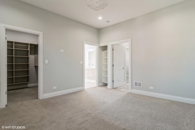 unfurnished bedroom with a walk in closet, light colored carpet, a closet, and ensuite bathroom