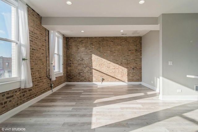 spare room featuring light wood-type flooring and brick wall