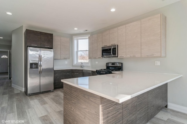 kitchen featuring stainless steel appliances, a breakfast bar area, light hardwood / wood-style floors, and kitchen peninsula