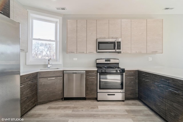 kitchen with appliances with stainless steel finishes, sink, and light wood-type flooring