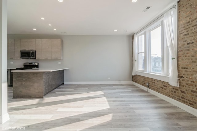 kitchen with brick wall, stainless steel appliances, kitchen peninsula, and light hardwood / wood-style flooring