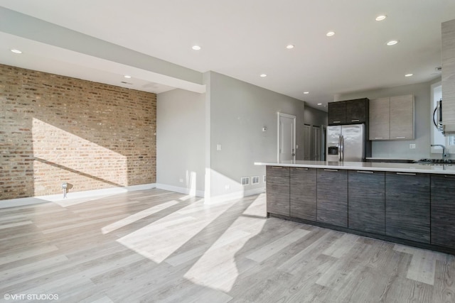 kitchen featuring brick wall, appliances with stainless steel finishes, and light hardwood / wood-style flooring