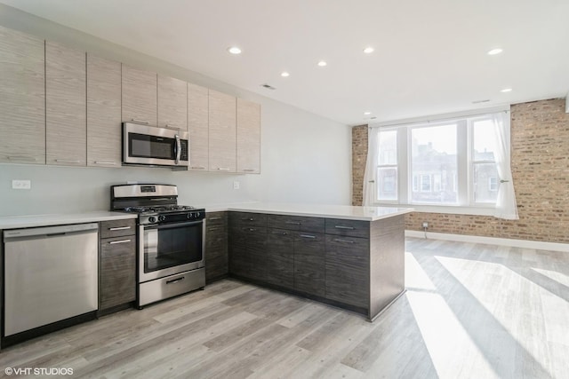 kitchen featuring stainless steel appliances, brick wall, light hardwood / wood-style flooring, and kitchen peninsula