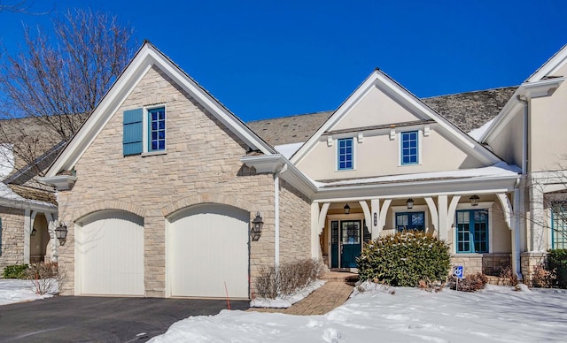 view of front of house with aphalt driveway, stucco siding, covered porch, a garage, and stone siding