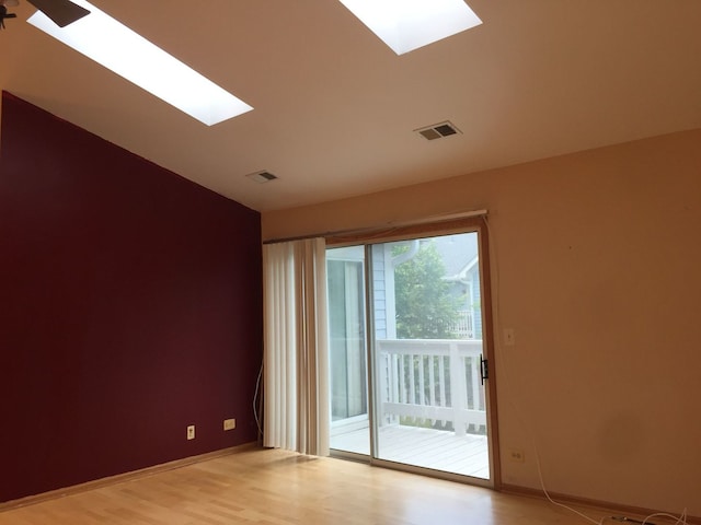 empty room featuring light wood-type flooring, a skylight, and visible vents