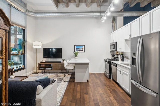 kitchen with dark hardwood / wood-style flooring, a towering ceiling, stainless steel appliances, decorative backsplash, and white cabinets