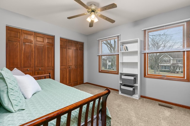 bedroom with multiple closets, light colored carpet, visible vents, a ceiling fan, and baseboards