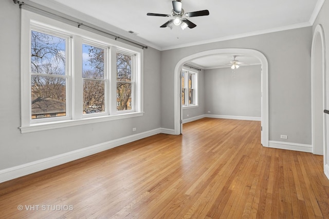 unfurnished room with arched walkways, visible vents, baseboards, ornamental molding, and light wood-type flooring