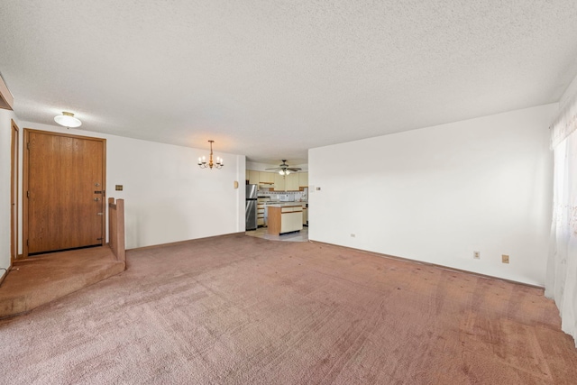 unfurnished living room with ceiling fan with notable chandelier, light colored carpet, baseboards, and a textured ceiling