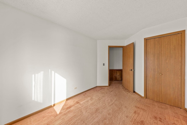 unfurnished bedroom with a closet, light colored carpet, a textured ceiling, and baseboards