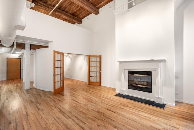 unfurnished living room featuring wooden ceiling, a fireplace with flush hearth, beamed ceiling, french doors, and light wood-style floors