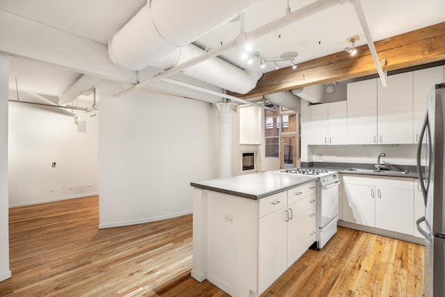 kitchen with dark countertops, white range with gas stovetop, white cabinets, and a sink