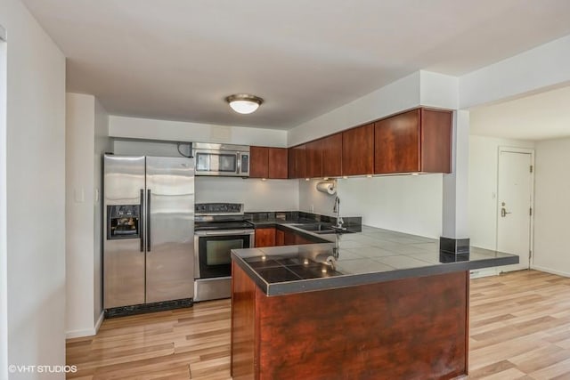 kitchen featuring stainless steel appliances, kitchen peninsula, sink, and light hardwood / wood-style flooring