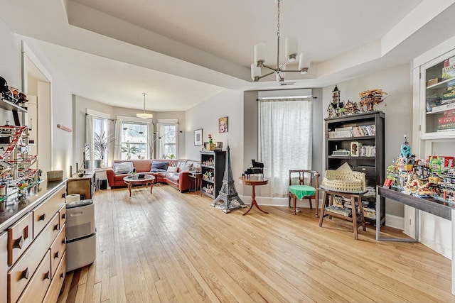 living area featuring light wood-style floors, a tray ceiling, baseboards, and an inviting chandelier