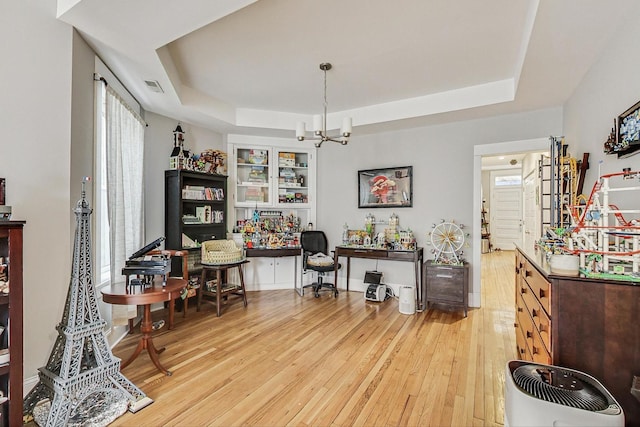 office with light wood-type flooring, a tray ceiling, visible vents, and a notable chandelier