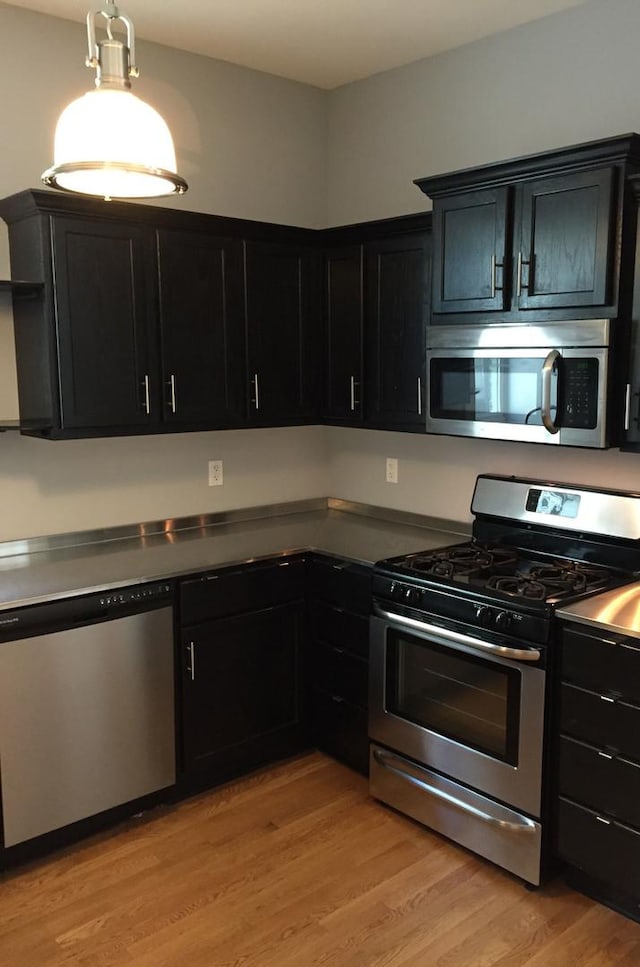 kitchen with open shelves, appliances with stainless steel finishes, light wood-type flooring, and dark cabinetry