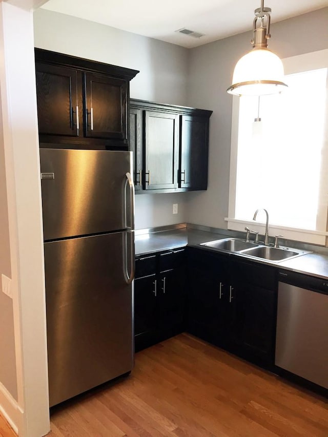 kitchen featuring visible vents, hanging light fixtures, stainless steel appliances, light wood-type flooring, and a sink