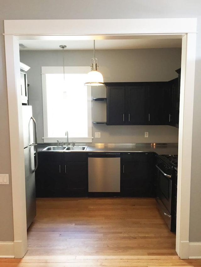 kitchen with appliances with stainless steel finishes, dark cabinets, light wood-type flooring, pendant lighting, and a sink