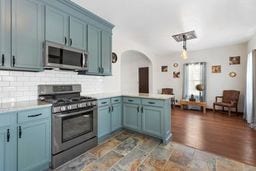 kitchen featuring a peninsula, light countertops, appliances with stainless steel finishes, blue cabinetry, and backsplash