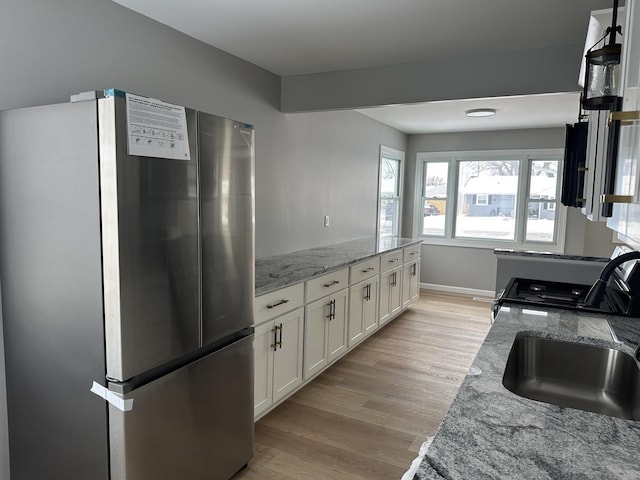 kitchen featuring light wood-style flooring, freestanding refrigerator, white cabinets, a sink, and light stone countertops