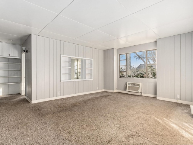 empty room with a wall mounted air conditioner, built in shelves, wood walls, and carpet