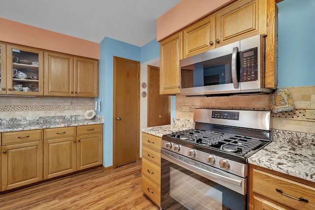 kitchen featuring stainless steel appliances, light stone countertops, light wood-type flooring, and decorative backsplash