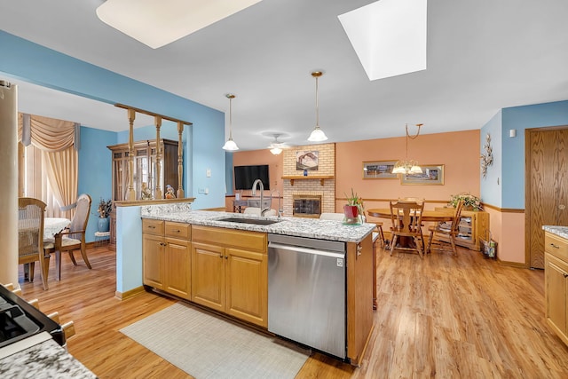 kitchen with sink, a brick fireplace, hanging light fixtures, dishwasher, and light hardwood / wood-style floors