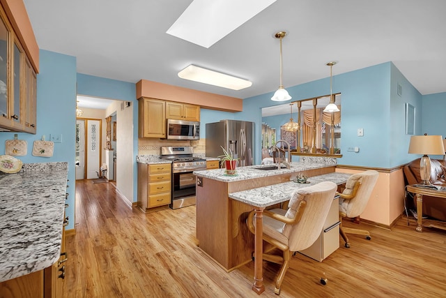 kitchen featuring a breakfast bar, sink, hanging light fixtures, appliances with stainless steel finishes, and light stone countertops