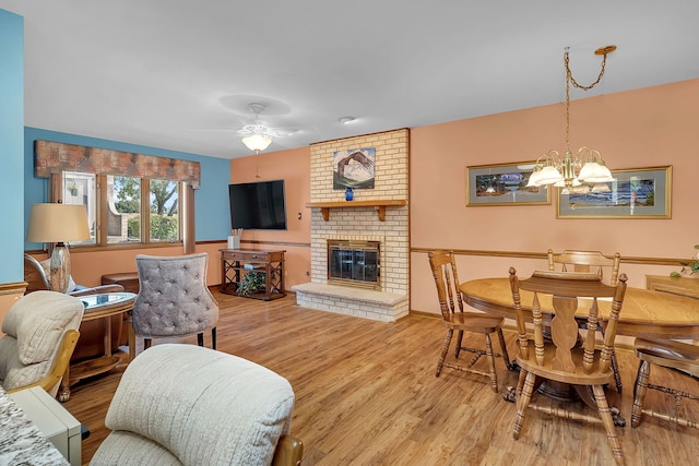 living room featuring a brick fireplace, ceiling fan with notable chandelier, and light hardwood / wood-style floors