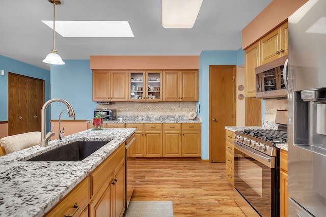 kitchen featuring appliances with stainless steel finishes, decorative light fixtures, sink, light stone countertops, and light wood-type flooring