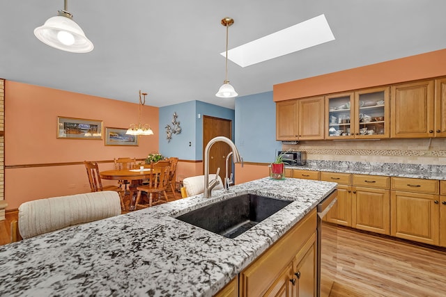 kitchen with light stone counters, light wood-type flooring, sink, and pendant lighting