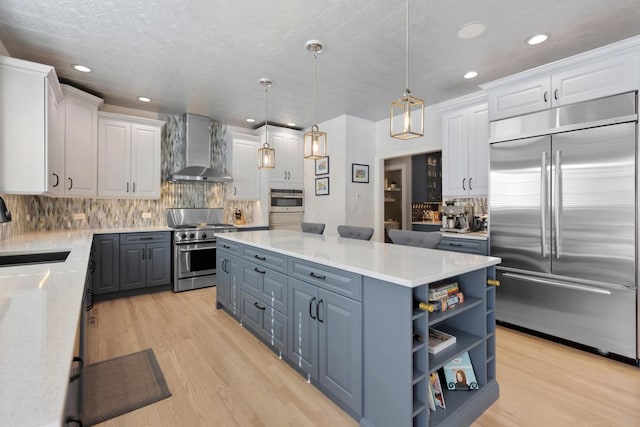 kitchen with stainless steel appliances, white cabinetry, a sink, and wall chimney exhaust hood