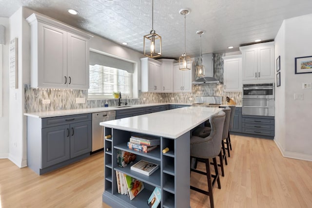 kitchen featuring gray cabinetry, wall chimney exhaust hood, a warming drawer, and stainless steel appliances