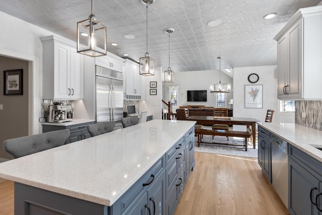 kitchen with a center island, light wood finished floors, stainless steel appliances, hanging light fixtures, and light stone countertops