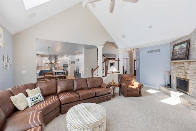 carpeted living room with stairs, decorative columns, a fireplace, visible vents, and ceiling fan with notable chandelier