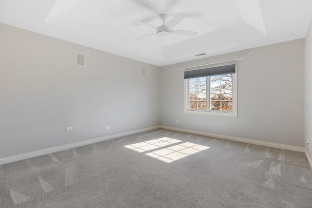 carpeted spare room with a ceiling fan, a raised ceiling, visible vents, and baseboards