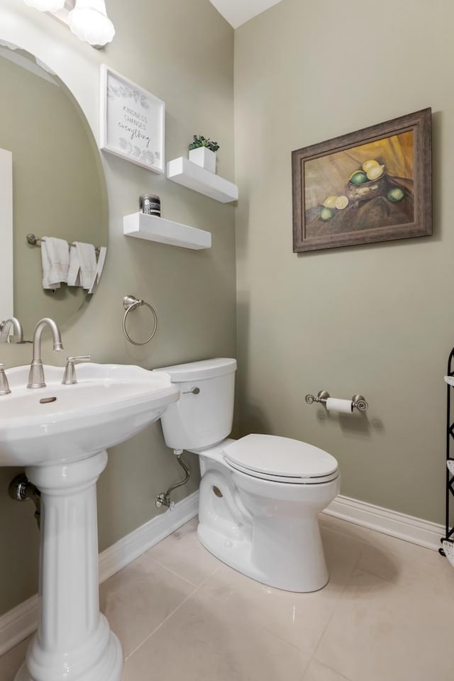 half bath with toilet, tile patterned flooring, baseboards, and a sink